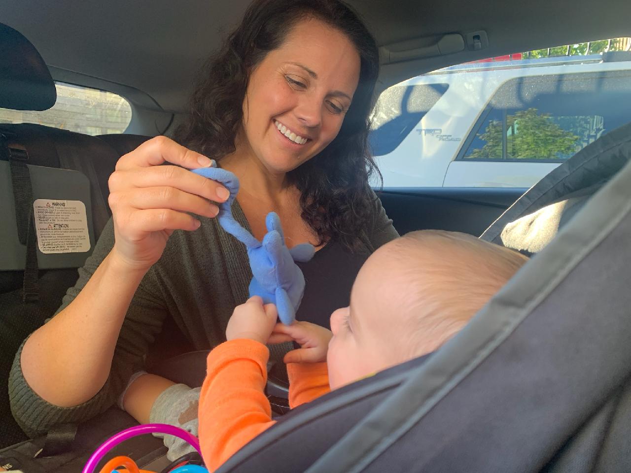 Mom holds up toy for baby in carseat to play with