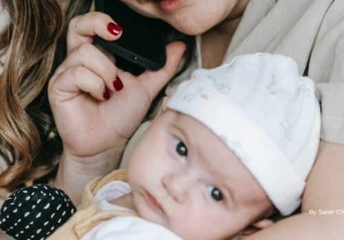 Infant looks off into the distance from the arms of his mother who is on her mobile phone. Photo by Sarah Chai on Pexels