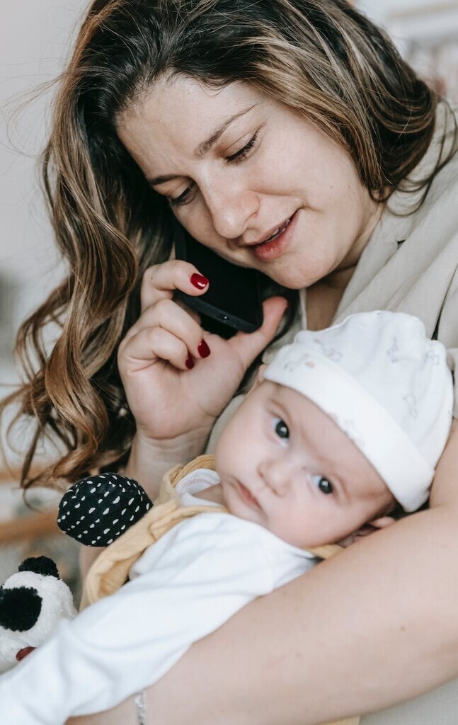 Mother talking on smartphone while holding baby who looks away from mother